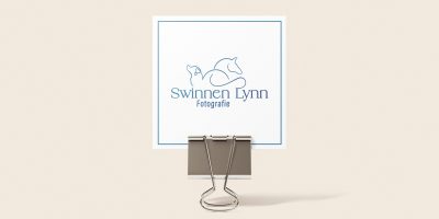 Visitekaartje voor Swinnen Lynn Fotografie, met een blauw lijnlogo van een paard en hond, vastgeklemd in een papierklem.